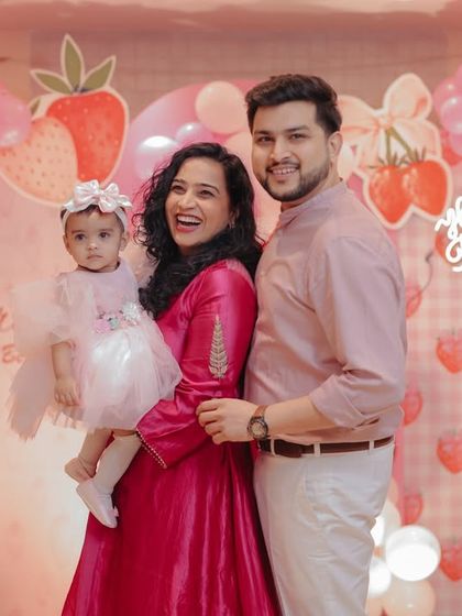 A classic family photo from Gauri's first birthday party. We are all smiling in front of the beautiful strawberry-themed decor, creating a perfect memory and a great promotional shot for the event vendors involved.