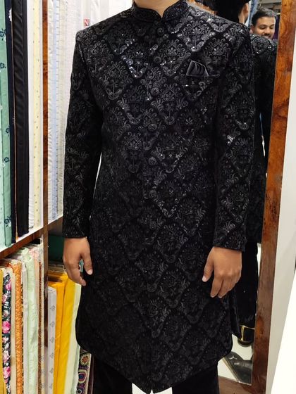 A groom trying on his black hand-worked sherwani in front of the mirror. The subtle sparkle of the embroidery catches the light beautifully.