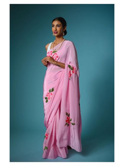 A full-length shot that captures the graceful fall of the pink saree's fabric. The simple styling keeps the focus on the product's beautiful hand-painted design.