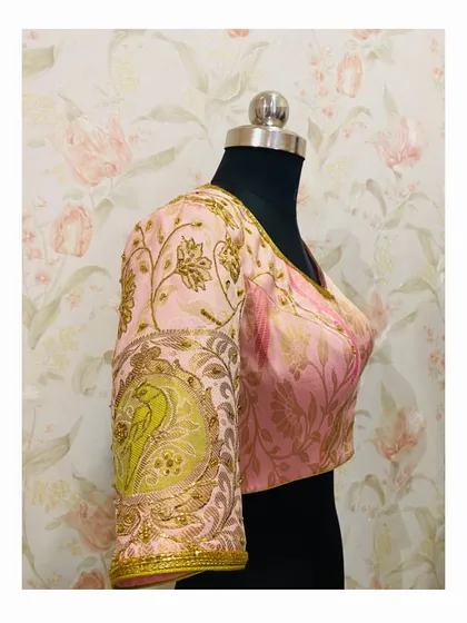 A detailed shot of a hand-embroidered sleeve, featuring a large peacock motif created with zardosi and threadwork on a pink brocade base.