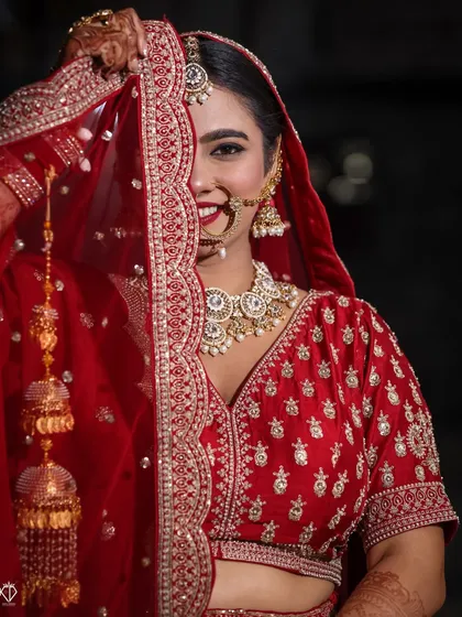 A playful and classic bridal pose. The bride peeking from behind her red dupatta, with a bright smile, captures her joyful spirit.