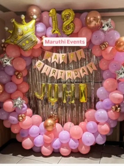 A sweet 18th birthday party with a circular balloon arch in pink and purple. A large crown balloon and foil letter balloons for the name add a special touch.
