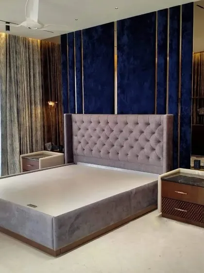 A luxurious, fully upholstered bed with a tall, button-tufted wingback headboard. The deep blue velvet wall paneling with metal inlays was also part of the project, creating a dramatic and high-end look for this master bedroom.