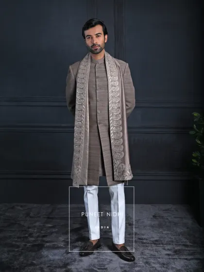 Minimal yet majestic, this brown matka silk achkan carries quiet strength. The stole, adorned with shimmering paisleys, introduces heritage detail, while ivory trousers offer crisp sophistication.