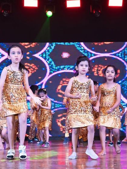 Young performers in sequined costumes at their annual dance show. The stage is brightly lit, and the colorful, abstract visuals on the LED screen add to the fun atmosphere.