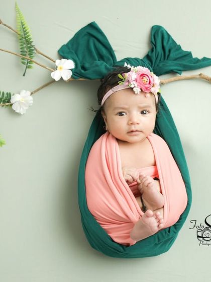 A creative "hanging cocoon" pose, where the baby is safely and comfortably wrapped to look like a little bud on a branch. It's a unique and artistic shot.