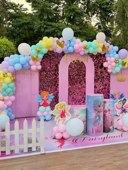 A beautiful Fairyland-themed birthday setup for an outdoor party. It features a pink castle backdrop with a shimmer panel, fairy cutouts, themed pedestals, and a pastel balloon arch.