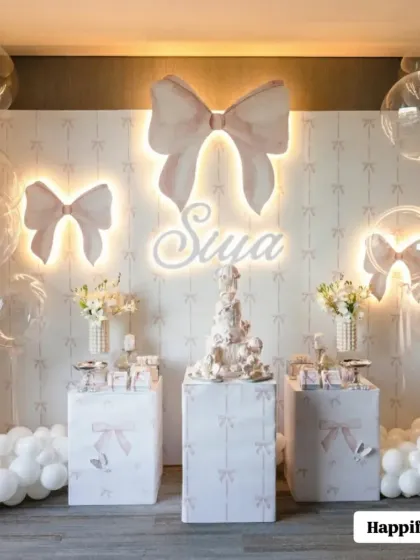 An elegant and dreamy setup for Siya's 6-month celebration, featuring a bow-themed backdrop with warm lighting, clear bubble balloons, and a beautiful dessert station.