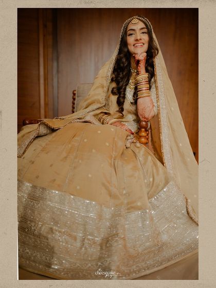 A happy and relaxed bride, seated and smiling, looking absolutely regal in her golden lehenga.
