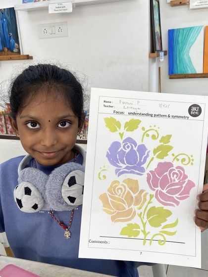 A student proudly holds up her beautiful floral stencil artwork. This activity helps children understand patterns, symmetry, and color combinations in a simple and engaging way.