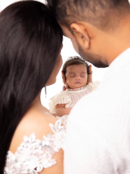 A creative over-the-shoulder shot focusing on the tiny newborn held securely in her parents' loving gaze. This is a beautiful way to capture the beginning of forever.