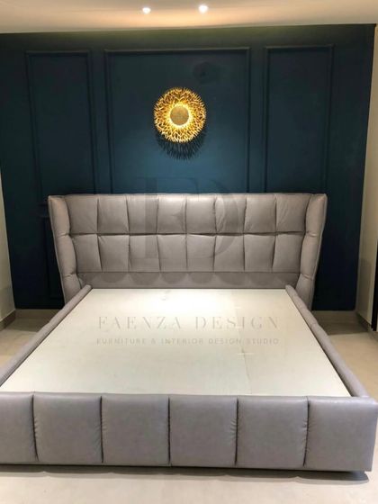 This grey tufted bed with a winged headboard is set against a deep teal paneled wall, creating a bold and dramatic contrast. The gold sunburst mirror adds a final decorative touch.