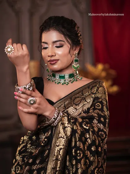 A full shot of the model adjusting her jewelry, showing the complete styling for the elegant black saree look.