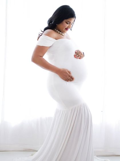 A classic silhouette portrait against a bright window. The mom-to-be's form is beautifully outlined in a simple white gown.