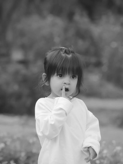 "Shhh." A little girl puts her finger to her lips in this classic black and white outdoor portrait. This style creates a timeless, storytelling feel.
