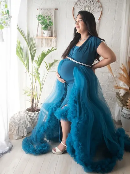 A beautiful standing portrait in a teal gown. The boho setup with its white brick wall, pampas grass, and hanging plants provides a fresh and stylish backdrop.