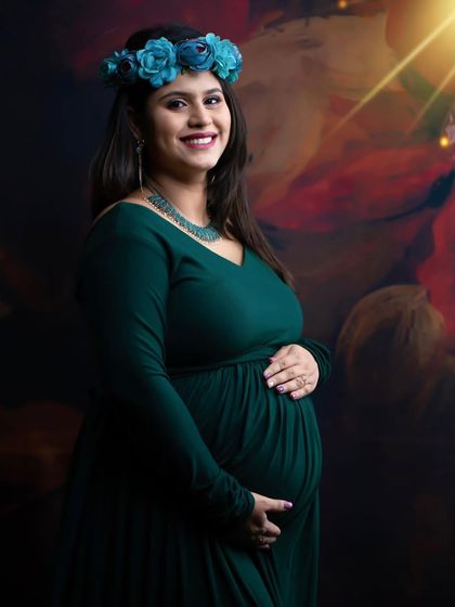 A lovely portrait with a soft, artistic light flare. The mom-to-be, in a green gown and floral crown, looks radiant against the painted backdrop.