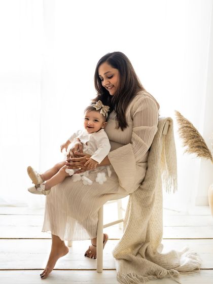 A mother and her six-month-old baby girl sharing a smile. The boho setup with pampas grass and soft fabrics adds a gentle, stylish touch to the portrait.