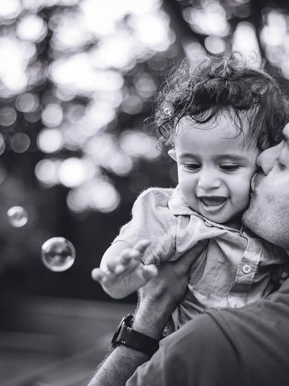 A father's tender kiss on his baby's cheek, captured in a beautiful black and white close-up with bubbles floating by.
