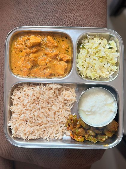 This balanced non-vegetarian thali features brown rice, chicken curry, sautéed cabbage, ivy gourd, and a side of curd.