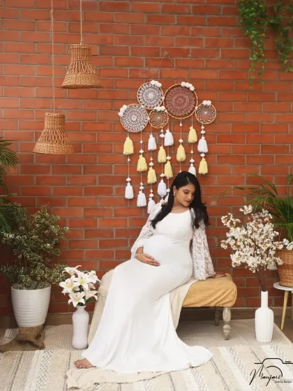 A serene and thoughtful pose, as she sits and cradles her bump. The cozy corner provides a peaceful and intimate backdrop.