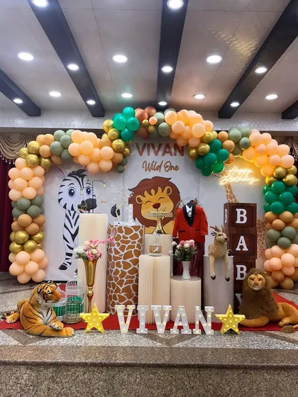 Welcome to the jungle! This "Wild One" themed birthday party is full of fun details. The setup includes a custom backdrop with cartoon lions and zebras, a lush balloon arch in safari colors, and plush animal props like a tiger and lion to bring the theme to life for the little one.