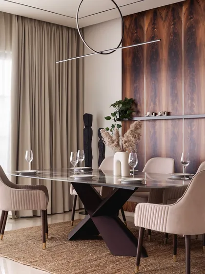 The dining area is defined by a stunning mahogany wood accent wall. The warm tones of the wood are complemented by the soft beige dining chairs and a modern, linear chandelier, creating an elegant space for entertaining.