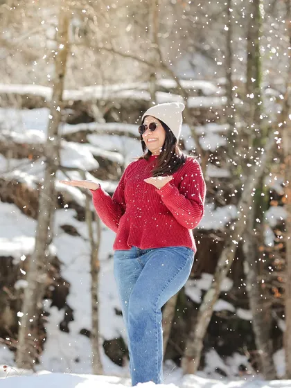 A joyful shot of the bride-to-be playing with snow in a sunlit forest.
