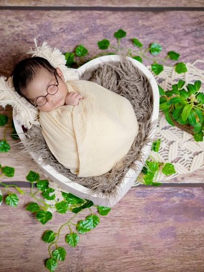 A wise little soul. This overhead shot shows a baby nestled in a heart-shaped bowl, surrounded by greenery for a natural, earthy look.