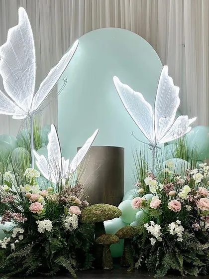 An elegant and artistic decor piece featuring large, illuminated butterflies nestled among flowers. These unique elements can transform any corner of your venue.