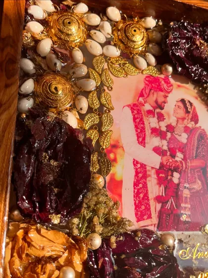 A detailed shot of a teakwood frame, showing the intricate placement of kaleera elements, supari, and varmala flowers around a couple's photo. Every detail is a piece of their story.