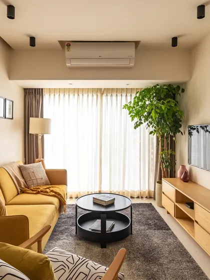 The living room, with its vibrant mustard sofa, abstract rug, and large planter. The space is a perfect blend of modern design and natural elements.