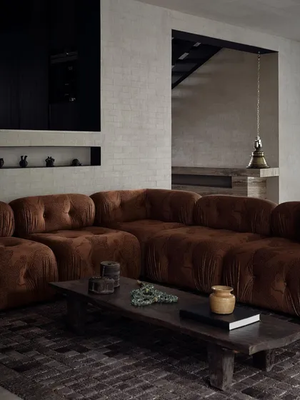 The living room, with its rich brown velvet sofa and dark wooden coffee table, is a cozy and inviting space. The traditional brass bell in the background adds a unique, cultural element.