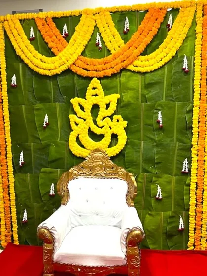 A traditional backdrop for a Half Saree ceremony. The setup features a wall of banana leaves, marigold garlands, and a floral Ganesha cutout.