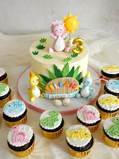 A truly 'Dino-mite' celebration for a third birthday. The friendly pink dinosaur on top of the cake is the main character, surrounded by a whole party of colorful dino friends on the matching cupcakes.