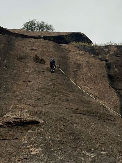 A lone climber rappels down a massive rock face in Ramanagara, showcasing the scale of the cliffs we train on.