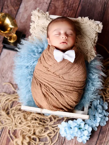 A sleeping newborn in a brown swaddle and a tiny white bowtie. This classic pose in a rustic crate is perfect for a timeless baby boy portrait.
