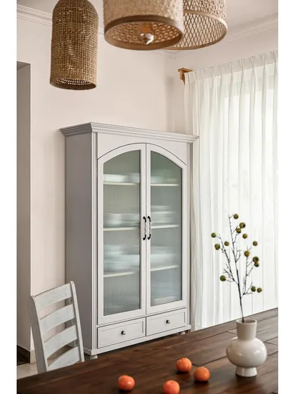 A close-up of the vintage-style crockery unit. The fluted glass doors and classic silhouette make it a statement piece that enhances the dining space's simple and minimal aesthetic.