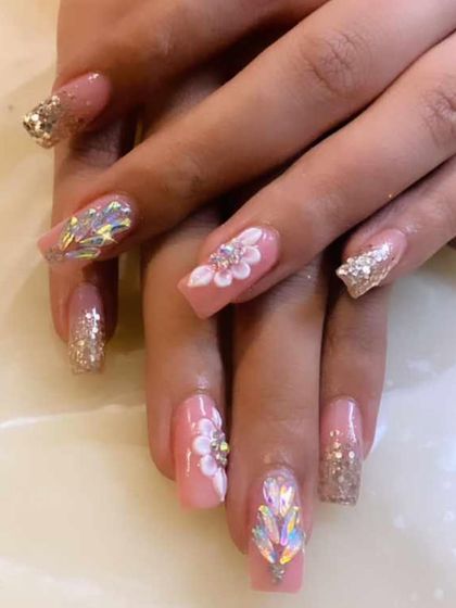 An incredibly detailed and luxurious set of pink extensions. It features 3D sculpted flowers, large iridescent crystals, and gold glitter accents for a truly show-stopping look.