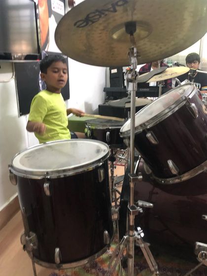 A young boy feels the power of an acoustic drum kit. While we often use electronic kits for classes, we ensure students also get experience on traditional drums.