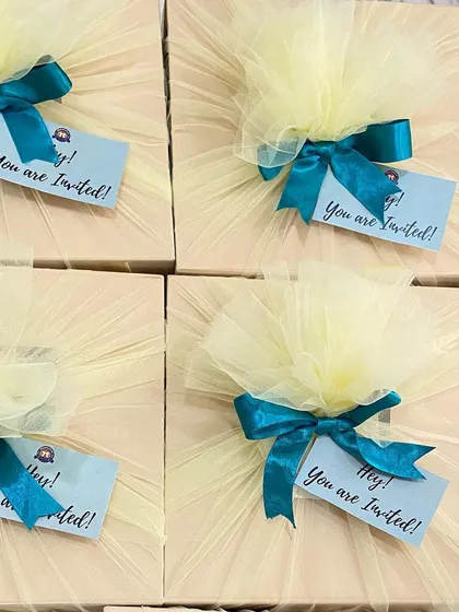 A pop of color makes any invitation more joyful. We used a bright yellow tulle wrap contrasted with a teal ribbon to create these fun and festive invitation gift boxes.