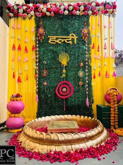 This Haldi backdrop combines a lush green wall with bright yellow drapes and traditional hangings. The brass urli is filled with rose petals, ready for the ceremony.