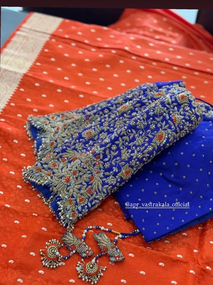 A vibrant contrast of a royal blue blouse with heavy all-over floral embroidery against a bright orange bandhani-style saree.