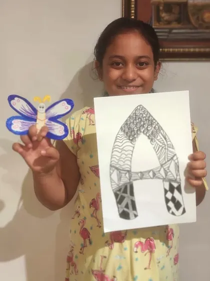 This student shows off two projects: a butterfly craft and a detailed zentangle drawing of the letter 'A'.