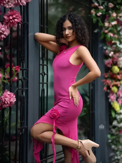 A confident pose in a bright pink dress, with the model leaning against a flower-adorned doorway. The colors are vibrant and the setting is perfect for a spring or summer fashion story.