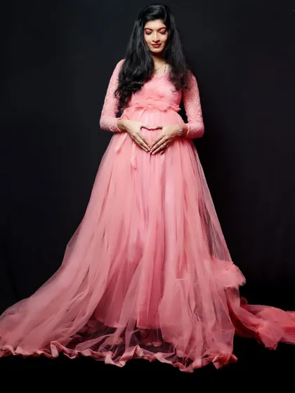 A simple and elegant studio portrait in a pink lace-sleeve maternity gown. The long train pools at the floor, creating a classic silhouette.