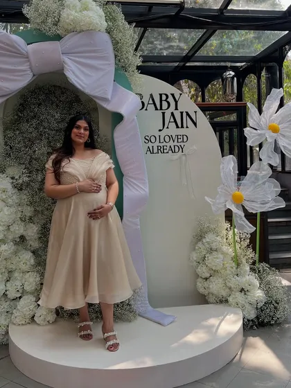 The beautiful mother-to-be posing in front of the custom backdrop we designed, filled with white florals and a giant bow.