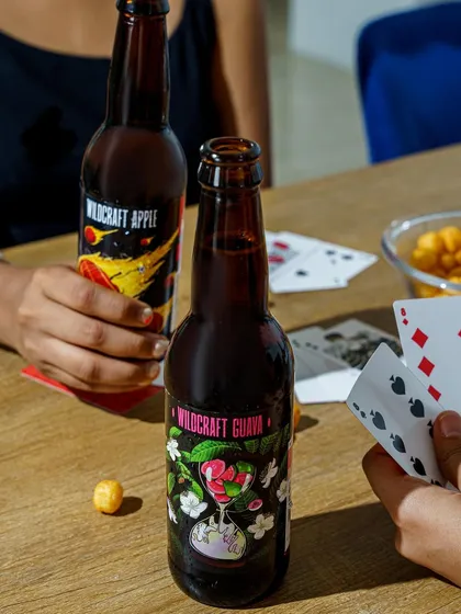 A lifestyle scene showing the product in a social context. People playing cards with bottles of Wildcraft on the table creates a relatable scenario of fun and relaxation, associating the brand with good times.