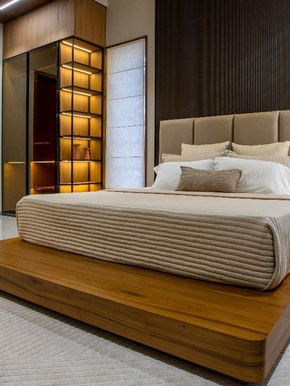 Detail of the platform bed and integrated storage solutions. The combination of a tufted headboard, ribbed wooden paneling, and illuminated glass wardrobe creates a look of understated luxury and high functionality.