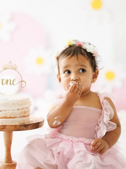 A close-up of the messy fun. With frosting on her face and fingers, this little one is fully enjoying her first birthday cake experience. These are the moments of pure, uninhibited joy.